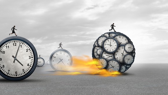 small stick figures race on large balls made of clocks with one with many clocks within it blazing ahead of the others. 
