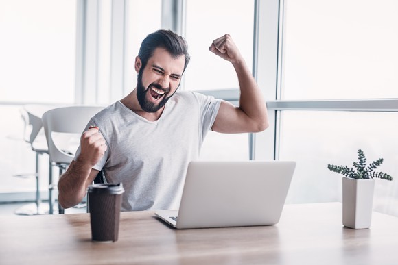 A man looking excited as he sits in front of a laptop.