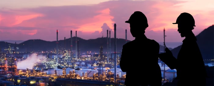 Workers look over an oil refinery site at sunset