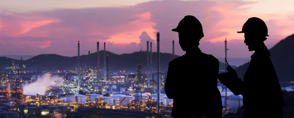 Workers look over an oil refinery site at sunset