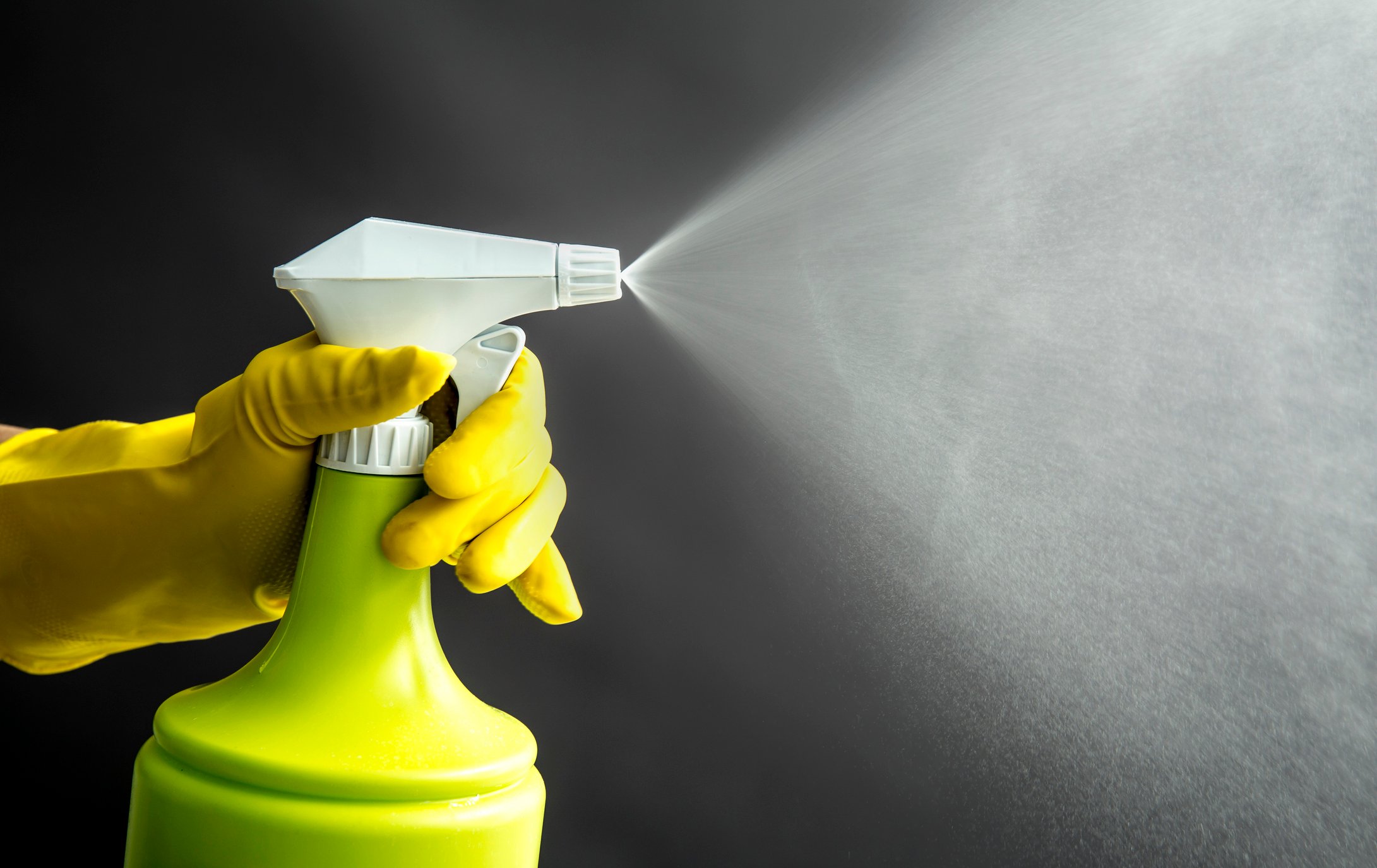 A hand wearing a rubber glove sprays  disinfectant  spray from left to right. 