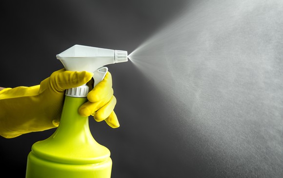 A hand wearing a rubber glove sprays  disinfectant  spray from left to right. 