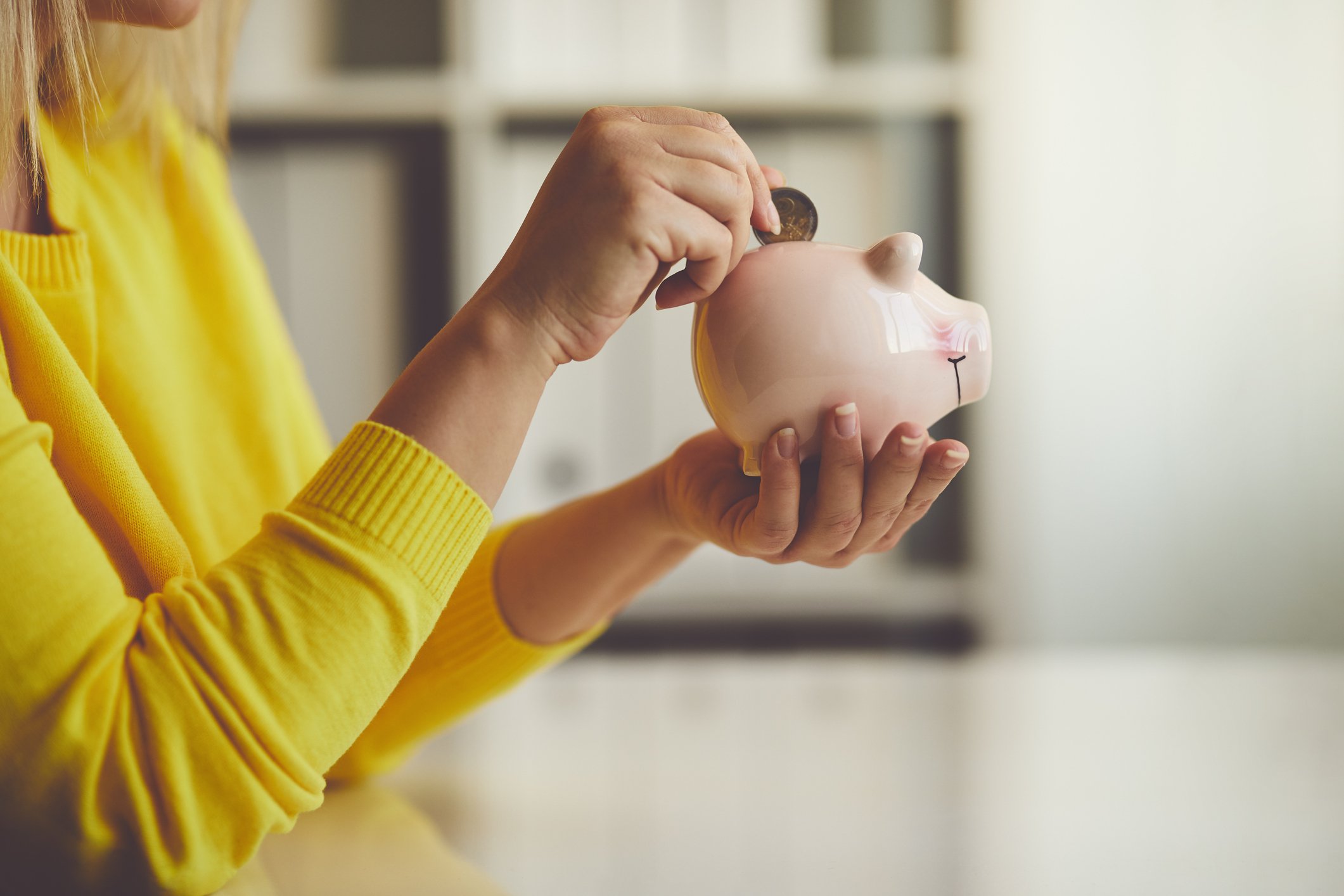 A woman placing a quarter in a piggy bank.