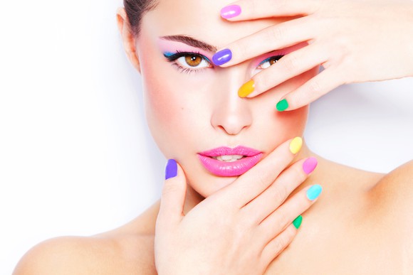 A female model wearing makeup holds her brightly-colored fingernails in front of her face.