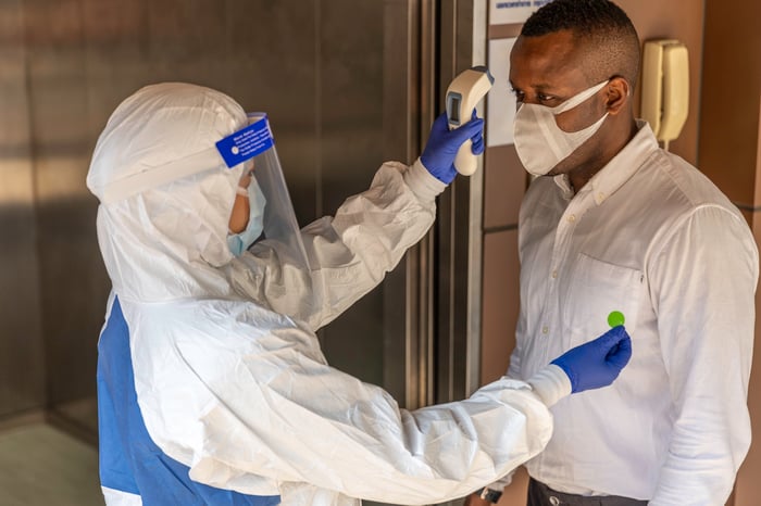 Guard in PPE suit uses infrared thermometer to check someone's temperature.