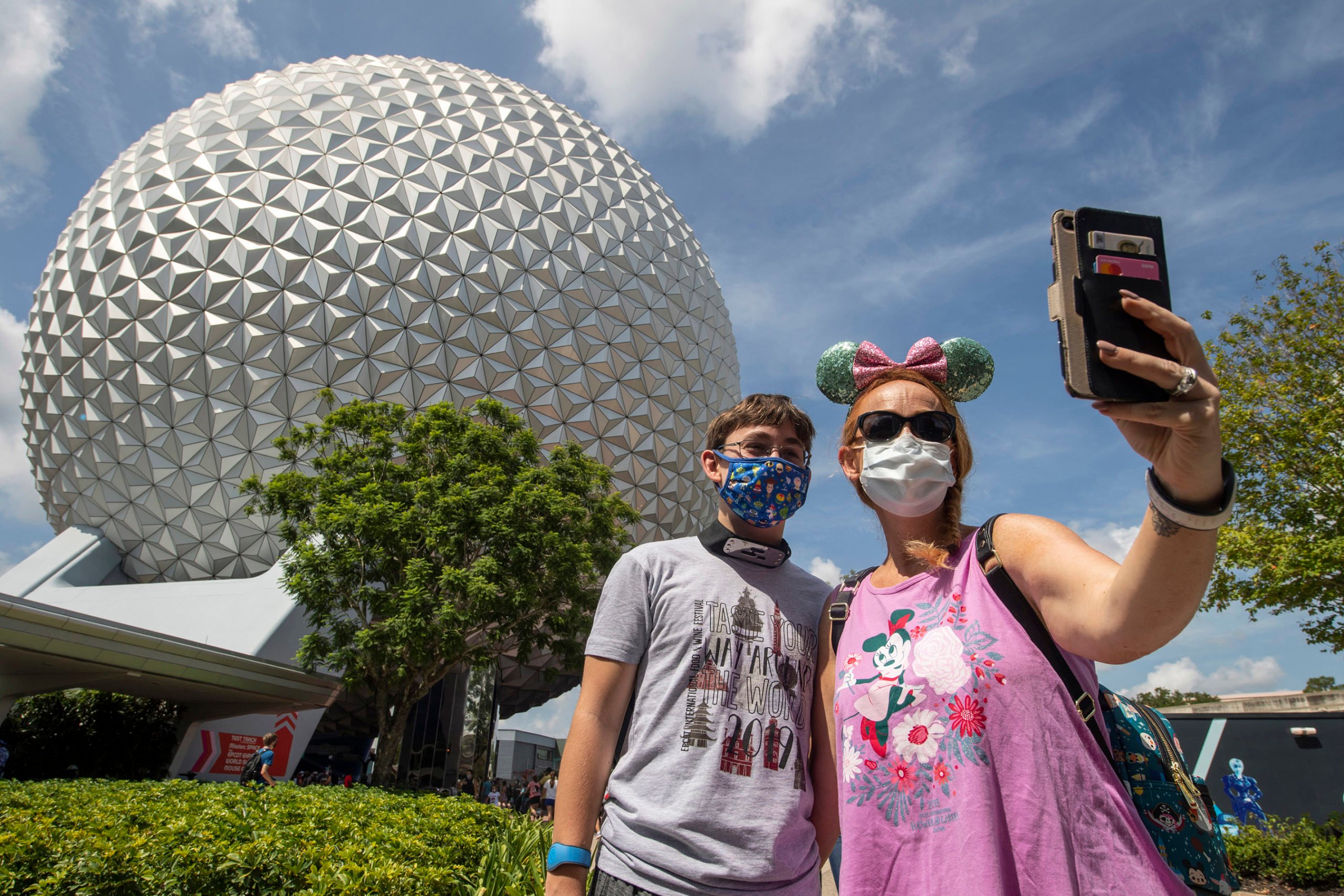 mother and son in protective face masks taking selfie in front of Epcot Center ball