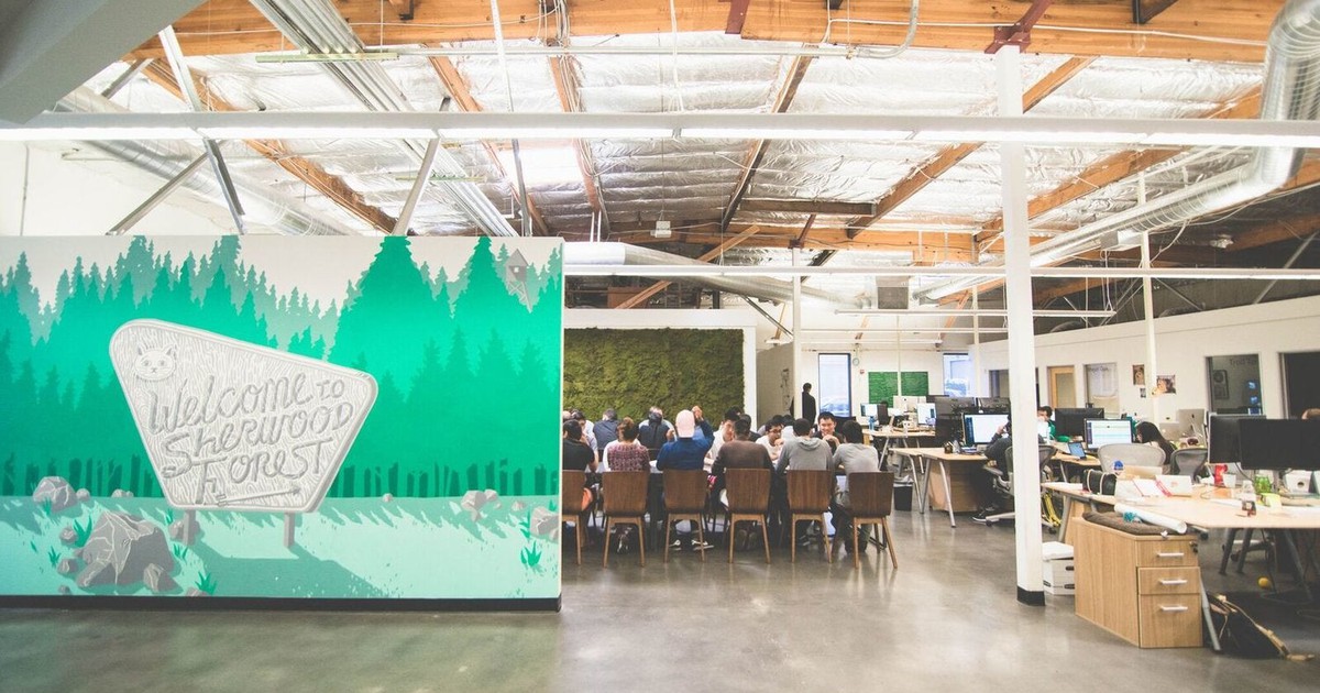 Office space with a green backdrop and a group of about a dozen people sitting around a conference table.