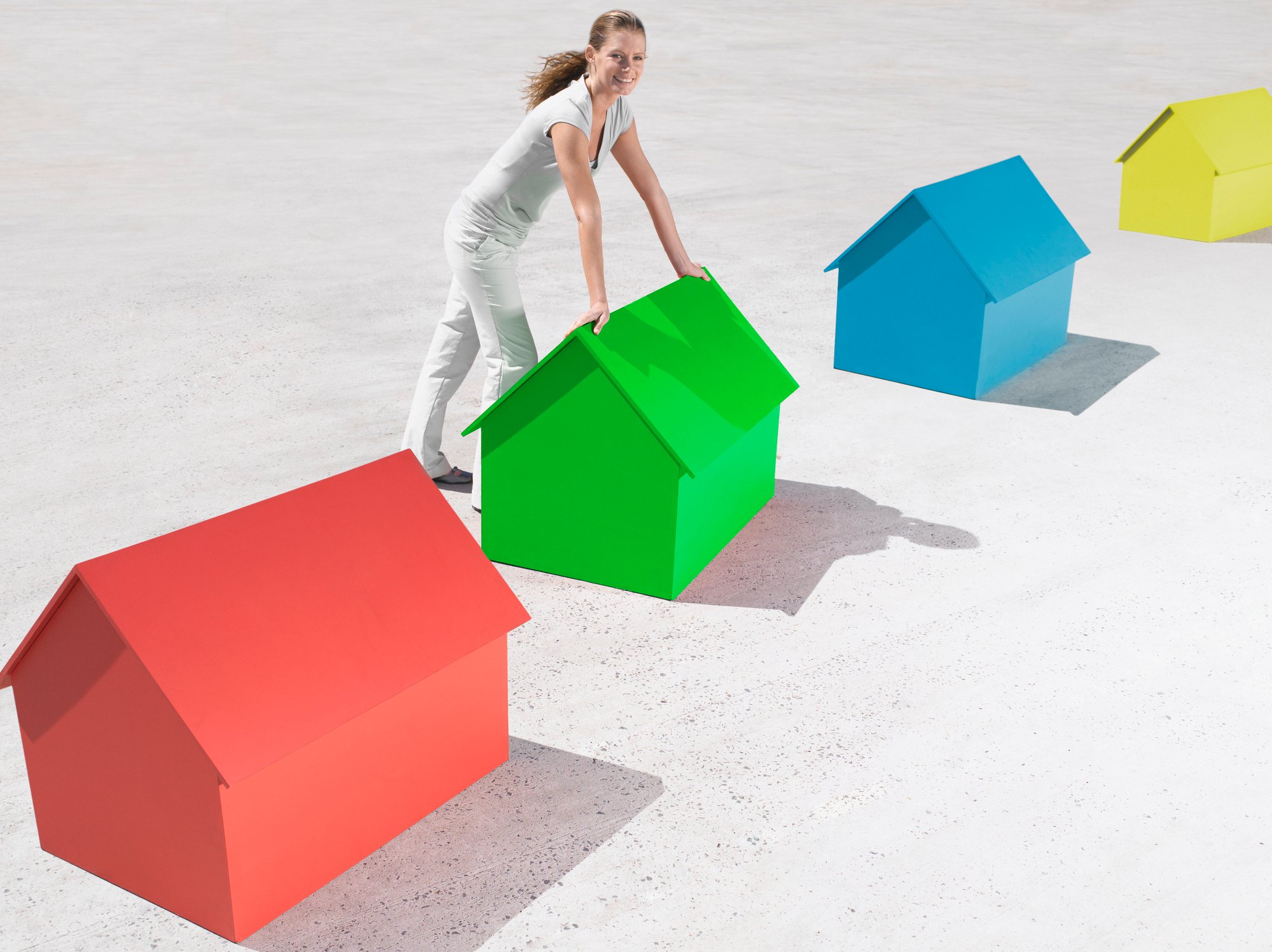 A woman dressed in white leaning forward on a small green house, which is in a row of multicolored small houses. 