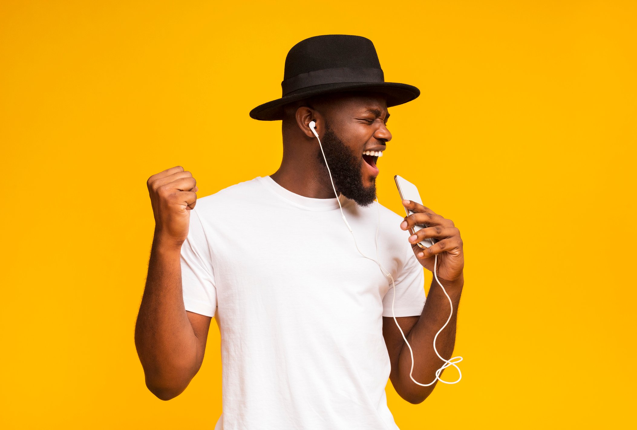 A man listens to music through headphones against an orange background.