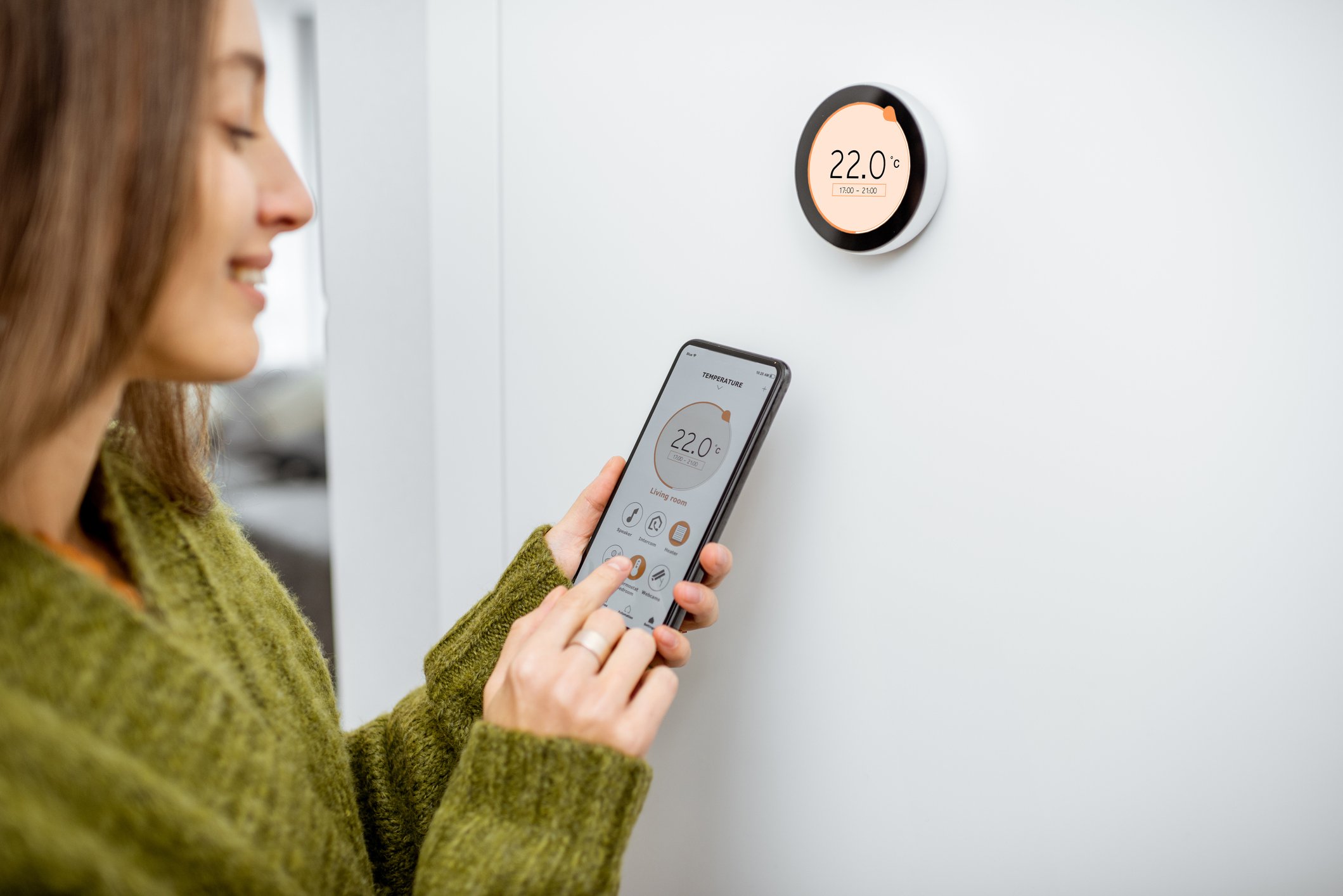 Woman adjusting a thermostat with a smartphone.