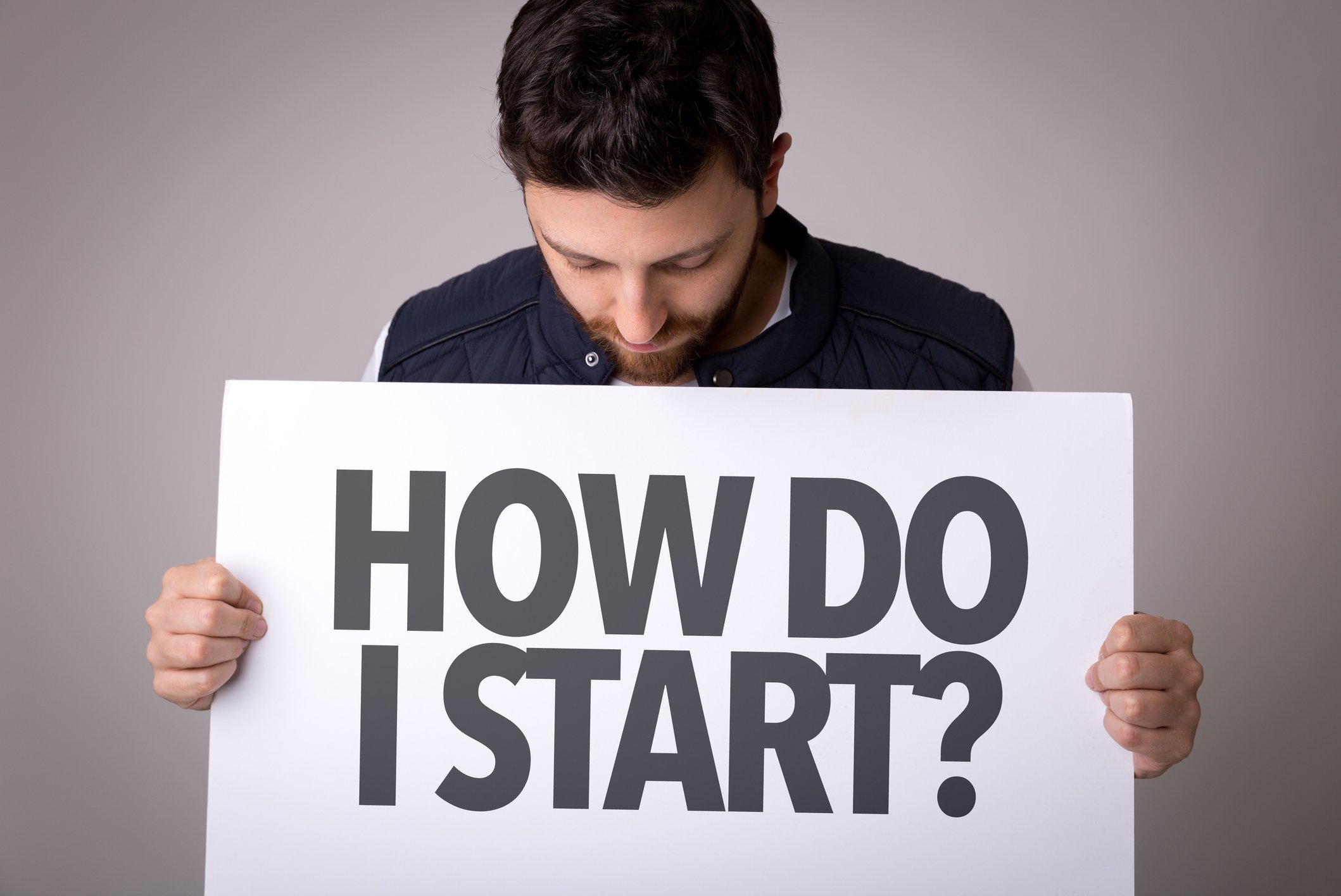 Man holding sign that reads, "how do I start?"