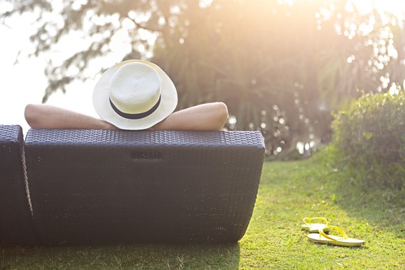 Viewed from back a person relaxes in a lounge chair outside with sandals on the ground next to him or her. 