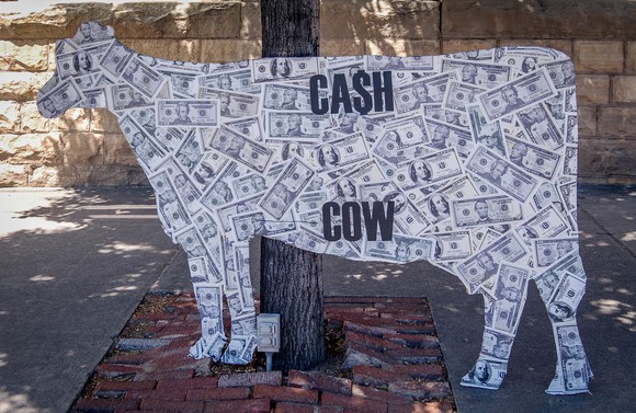 Cash stuck on a cutout shaped like a cow with the words "CA$H COW" 