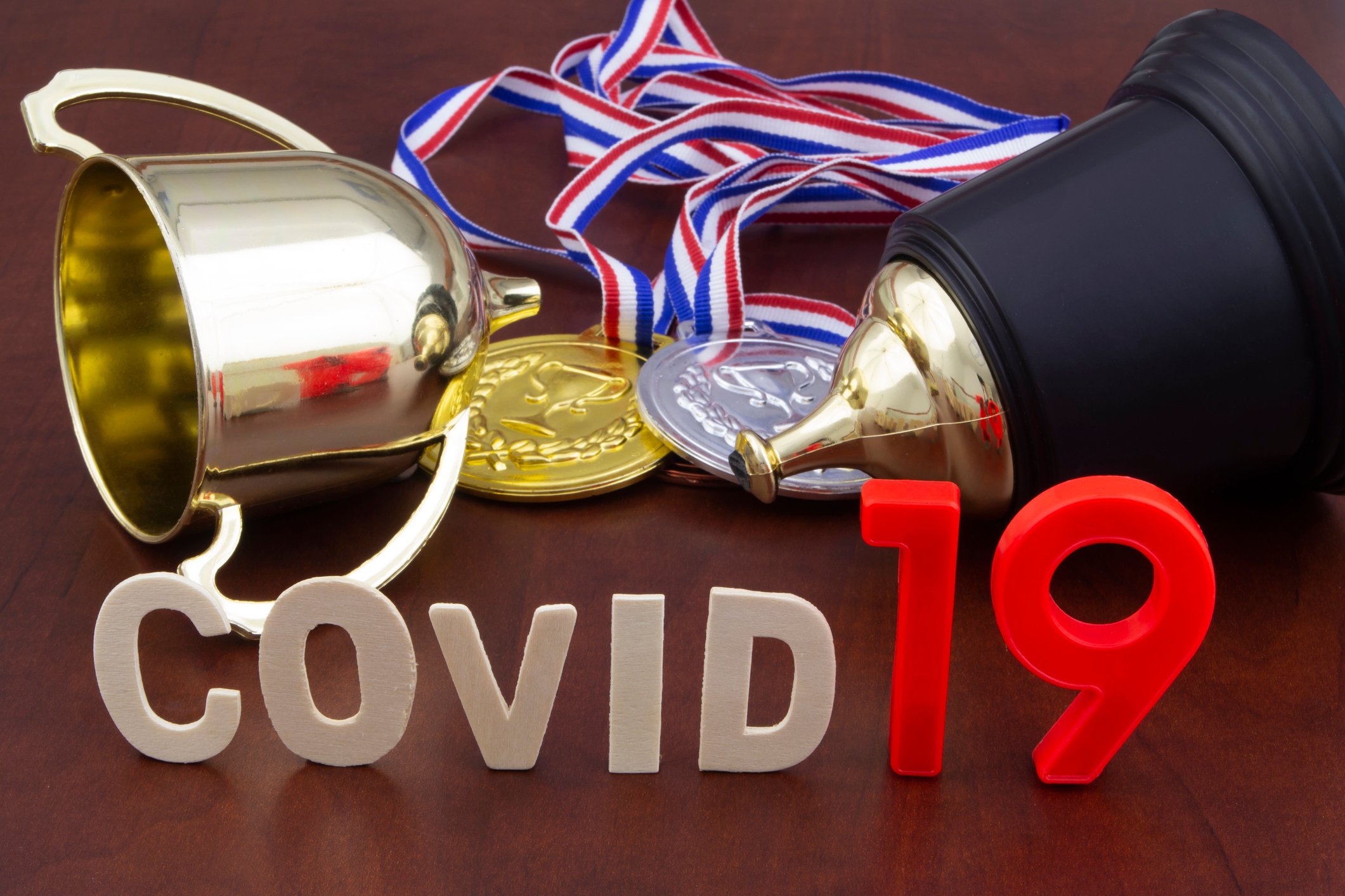 COVID-19 spelled out in front of a trophy, gold medal, and silver medal