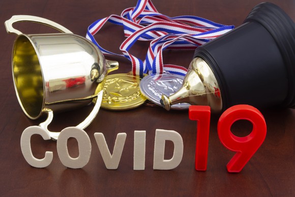 COVID-19 spelled out in front of a trophy, gold medal, and silver medal