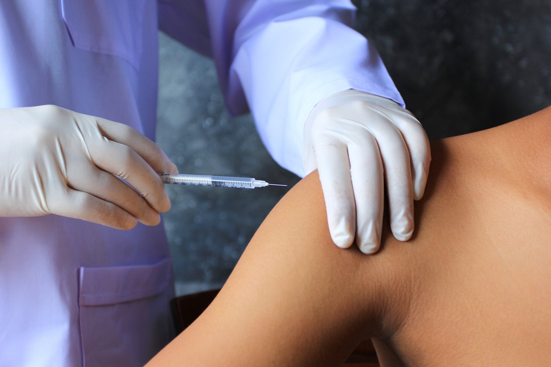 Gloved hands giving an injection into a shoulder.
