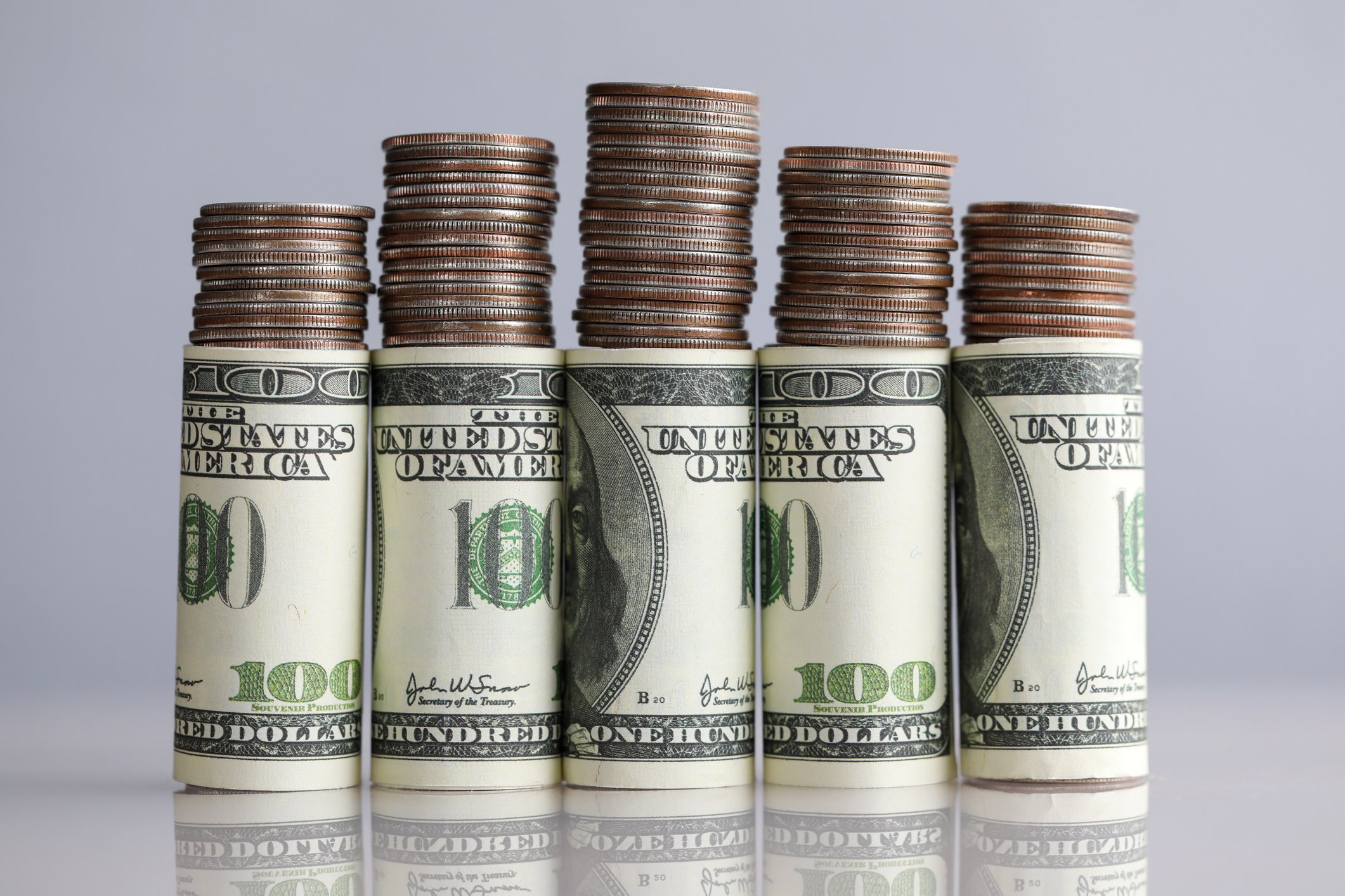 Stacks of coins on top of rolled hundred dollar bills