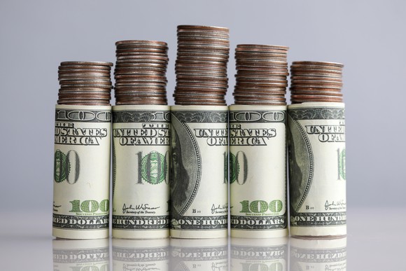 Stacks of coins on top of rolled hundred dollar bills