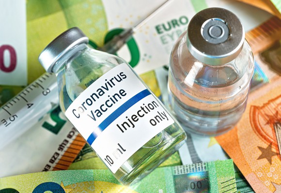 A pair of coronavirus vaccine vials sit on top of currency bills.