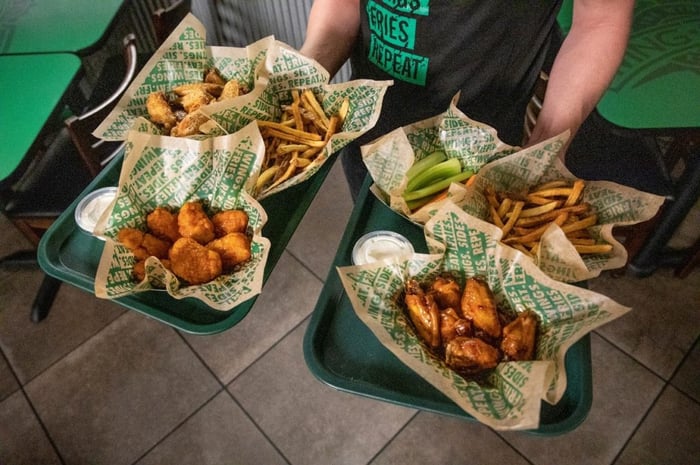 A Wingstop employee carries two trays holding baskets of chicken wings and french fries.