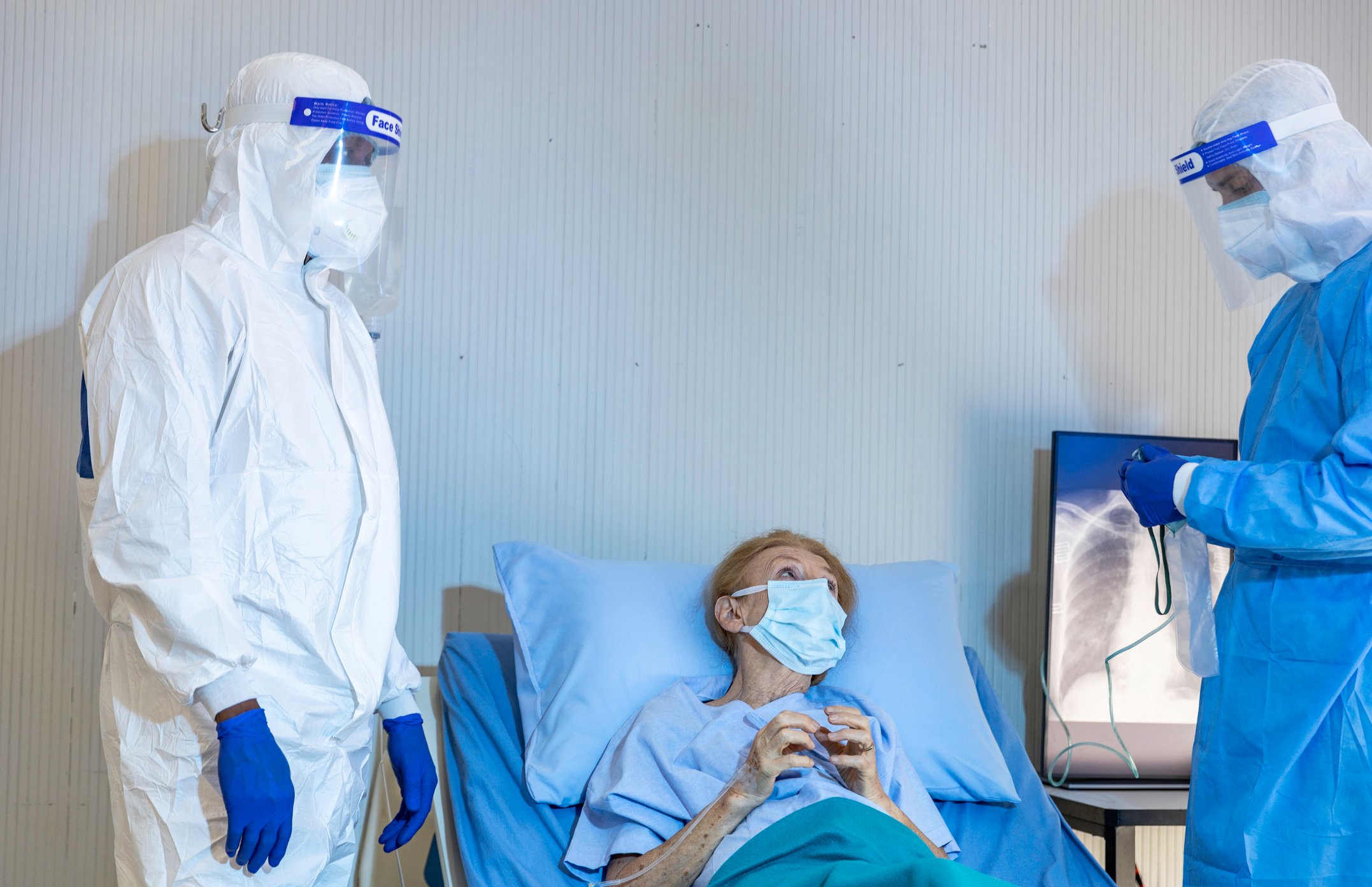 Doctors in personal protective equipment talking to an elderly patient in a bed