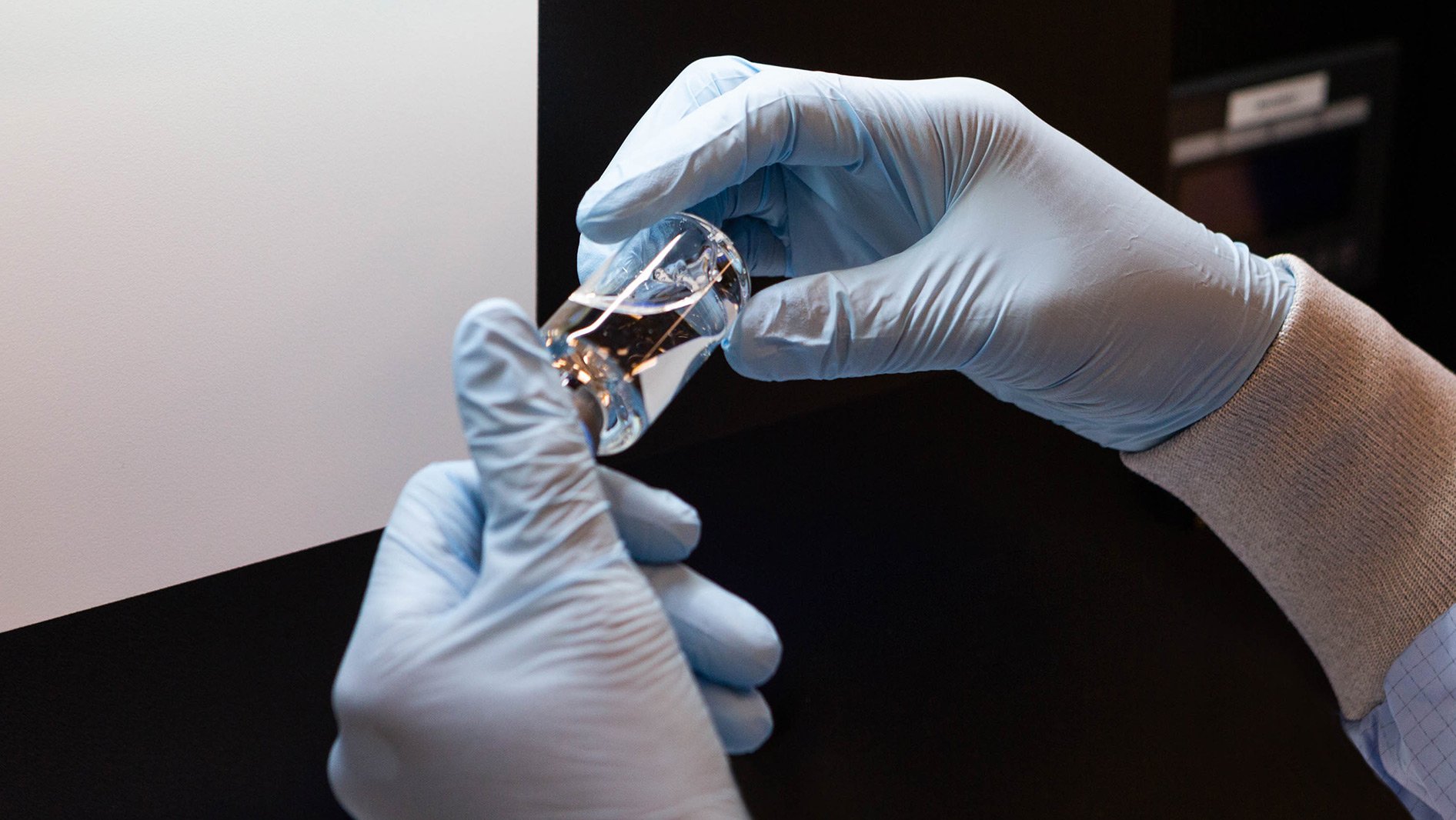 Gloved hands holding a vial of vaccine.