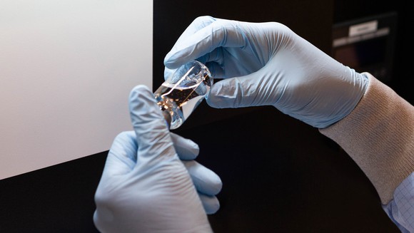 Gloved hands holding a vial of vaccine.