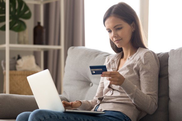 Young woman holding credit card in her left hand as she shops online.