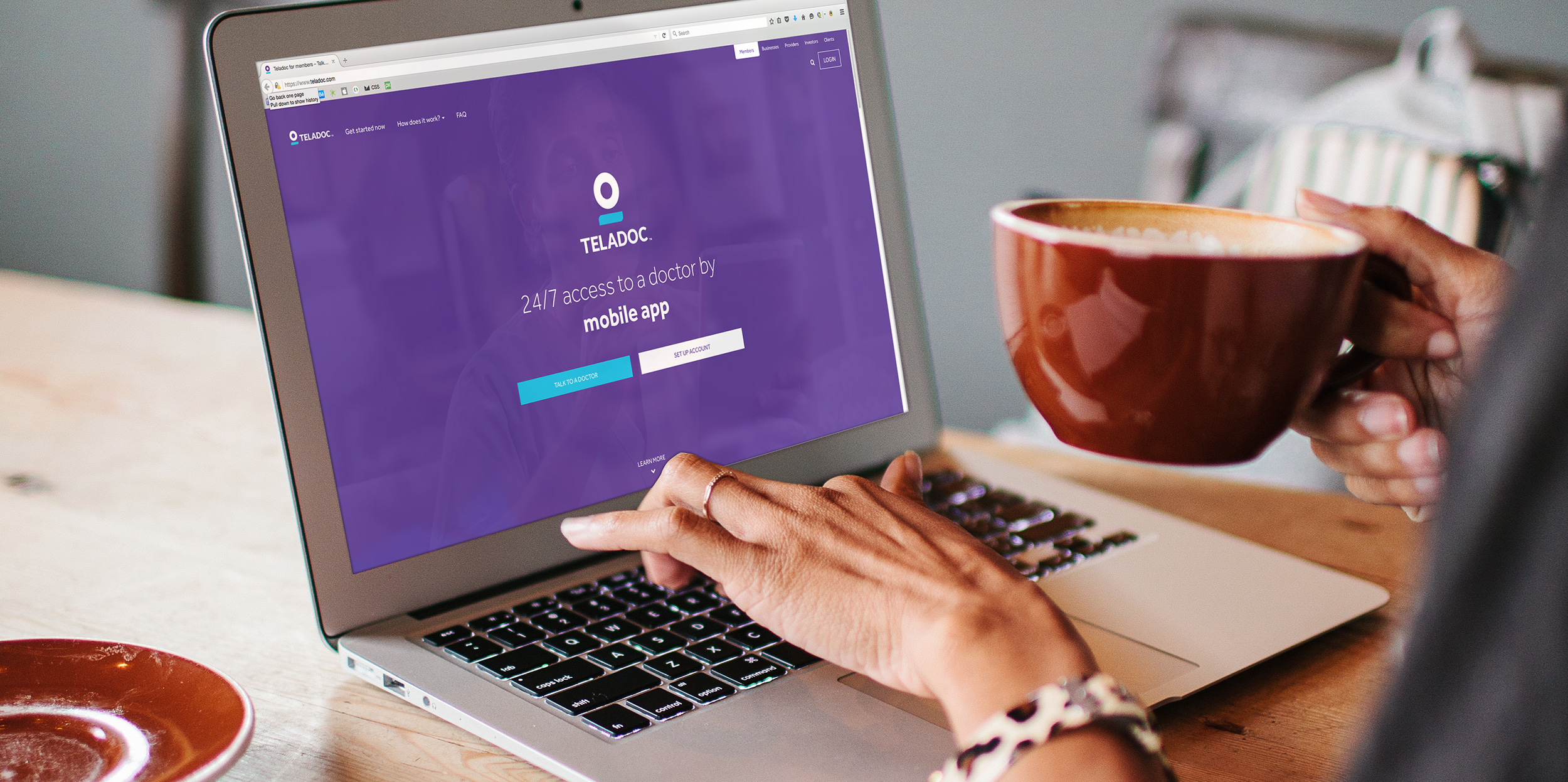 Woman accessing Teladoc services through laptop while holding a cup of coffee.