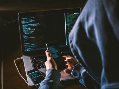 A hooded hacker using phones and a PC