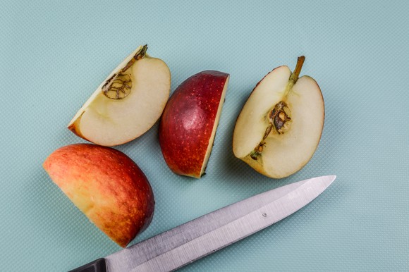 A knife placed below an apple cut into quarters.
