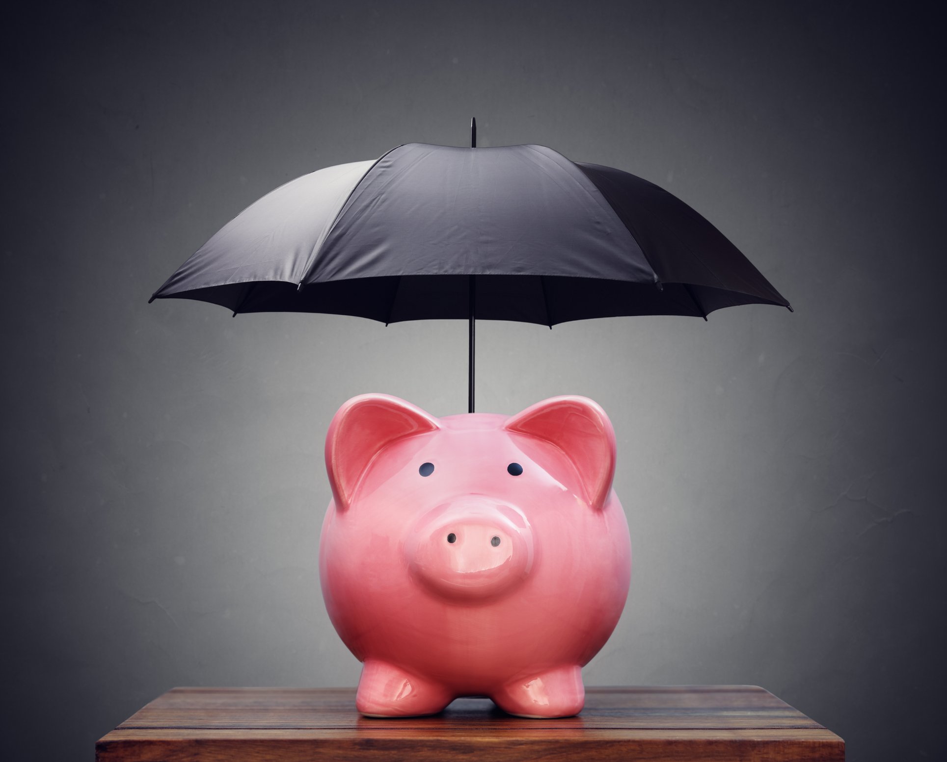 A piggy bank positioned below a black umbrella 