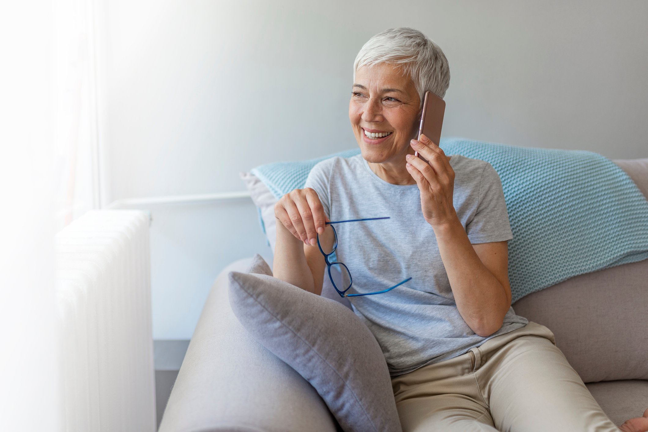 An older woman uses a smartphone while sitting on the couch.