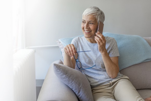 An older woman uses a smartphone while sitting on the couch.