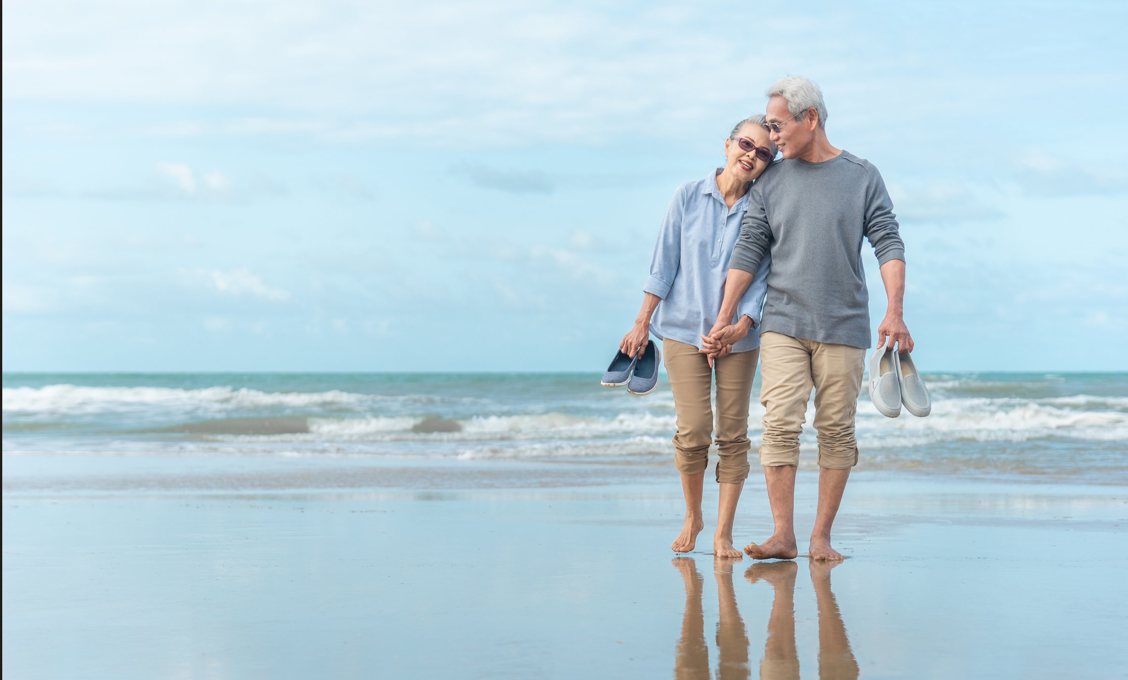 A couple of retirees walking hand in hand along the beach. 
