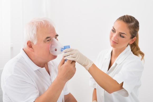 A medical professional looking at senior patient inhaling through oxygen mask.