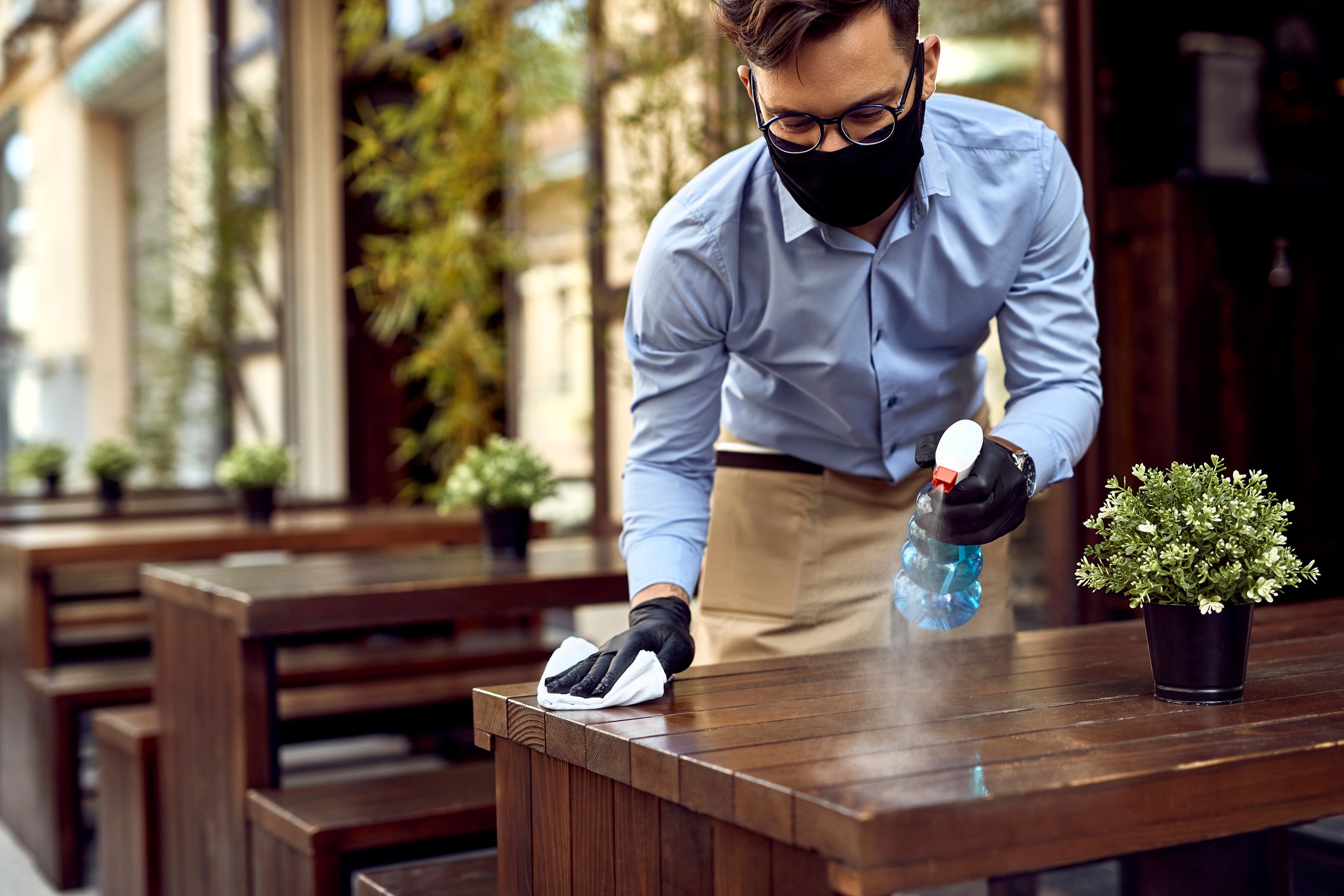 A waiter wears a mask and sprays disinfectant on the table. 