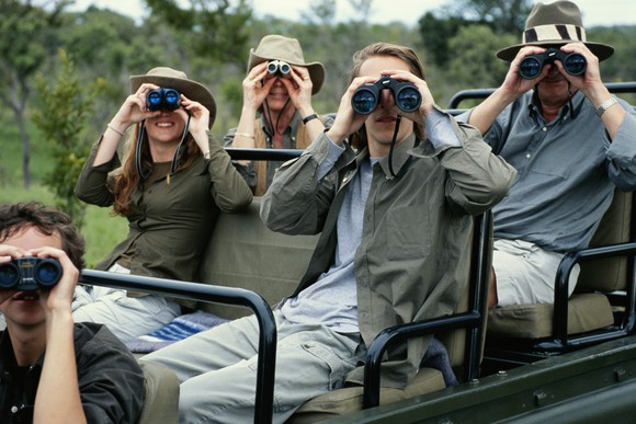 A traveling family sits on a Jeep and looks at camera with binoculars. 
