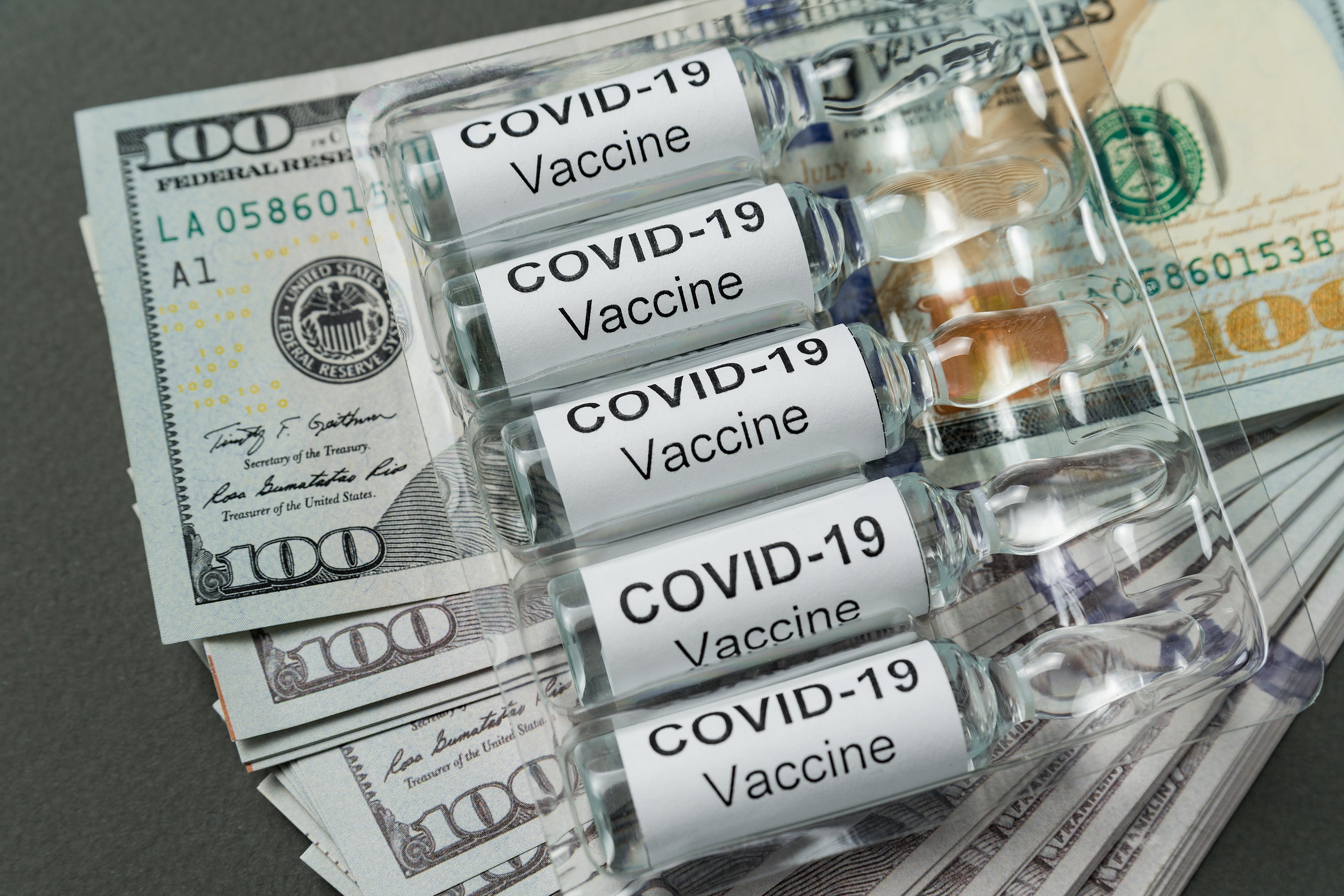 Bottles labeled covid 19 vaccine sit stop stacks of hundred dollar bills.