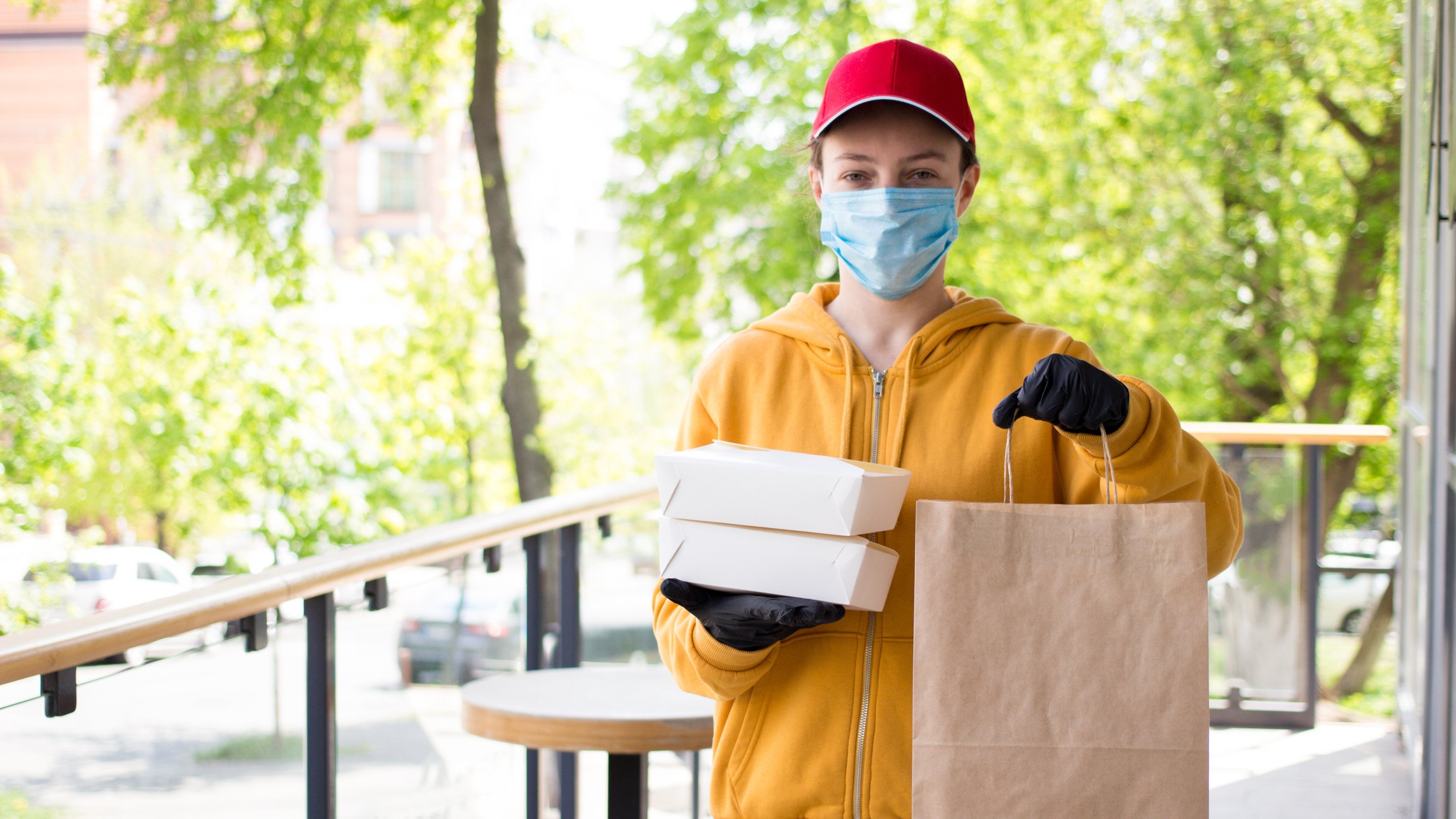 A food service employee delivers food while wearing a mask and gloves.