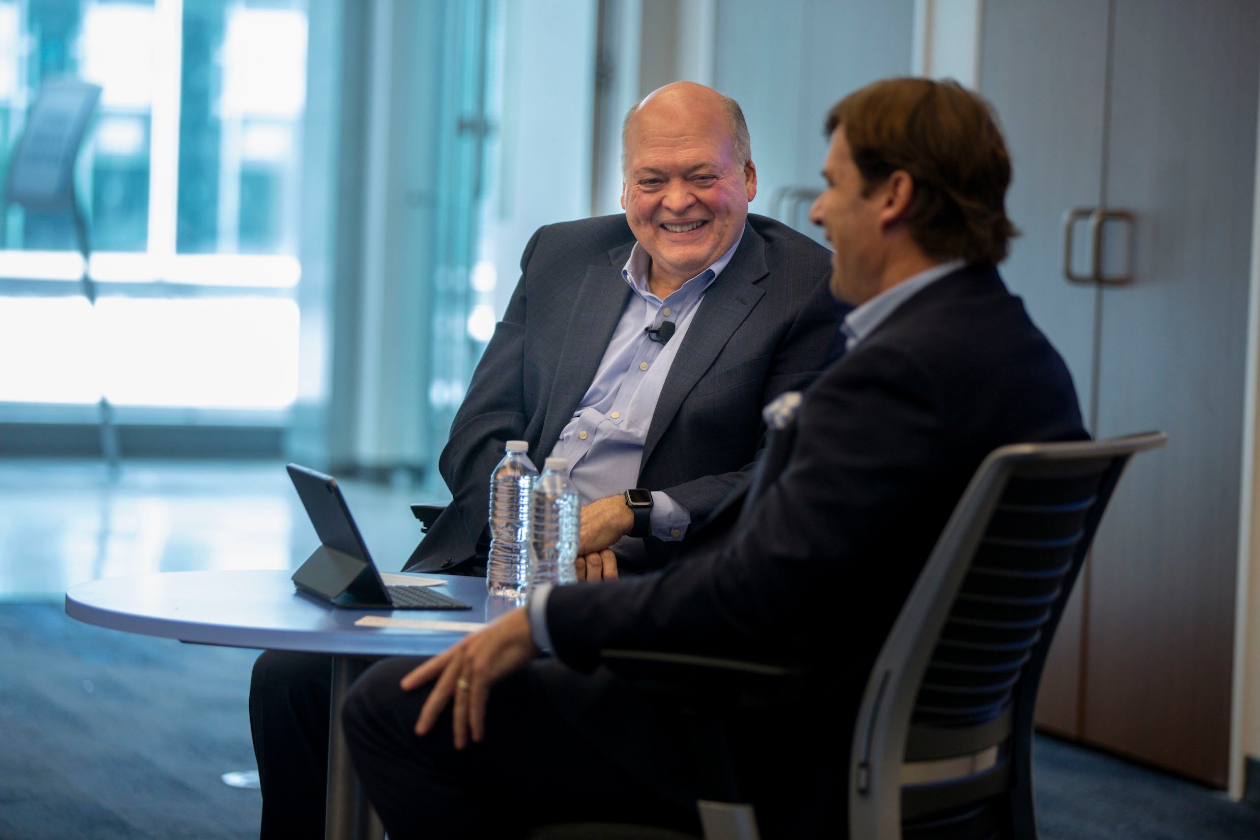 Hackett and Farley are shown seated at a table during a presentation. 