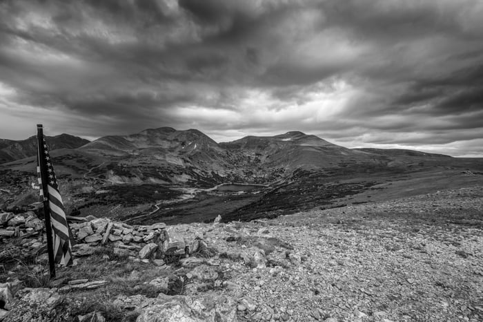 Desert landscape with American flag under a cloudy sky, all in black and white.