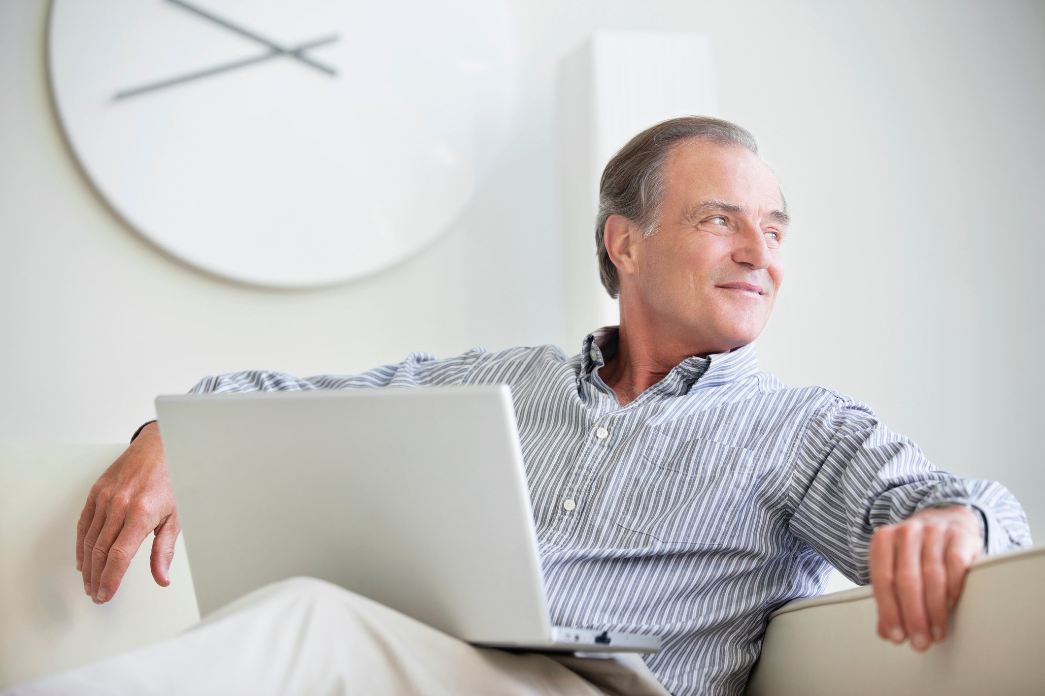 Man sitting on a couch looking out a window with a laptop on his lap