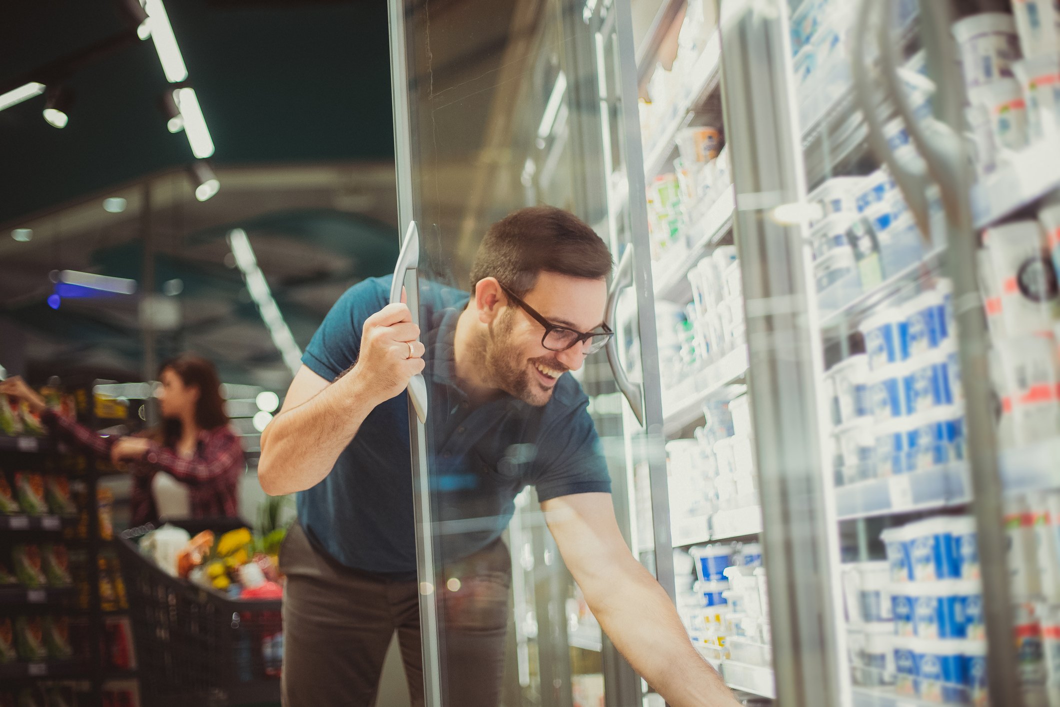 A man reaches into a refrigerator at the grocery store.