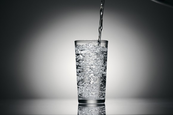 Sparkling water is poured into a tall glass.
