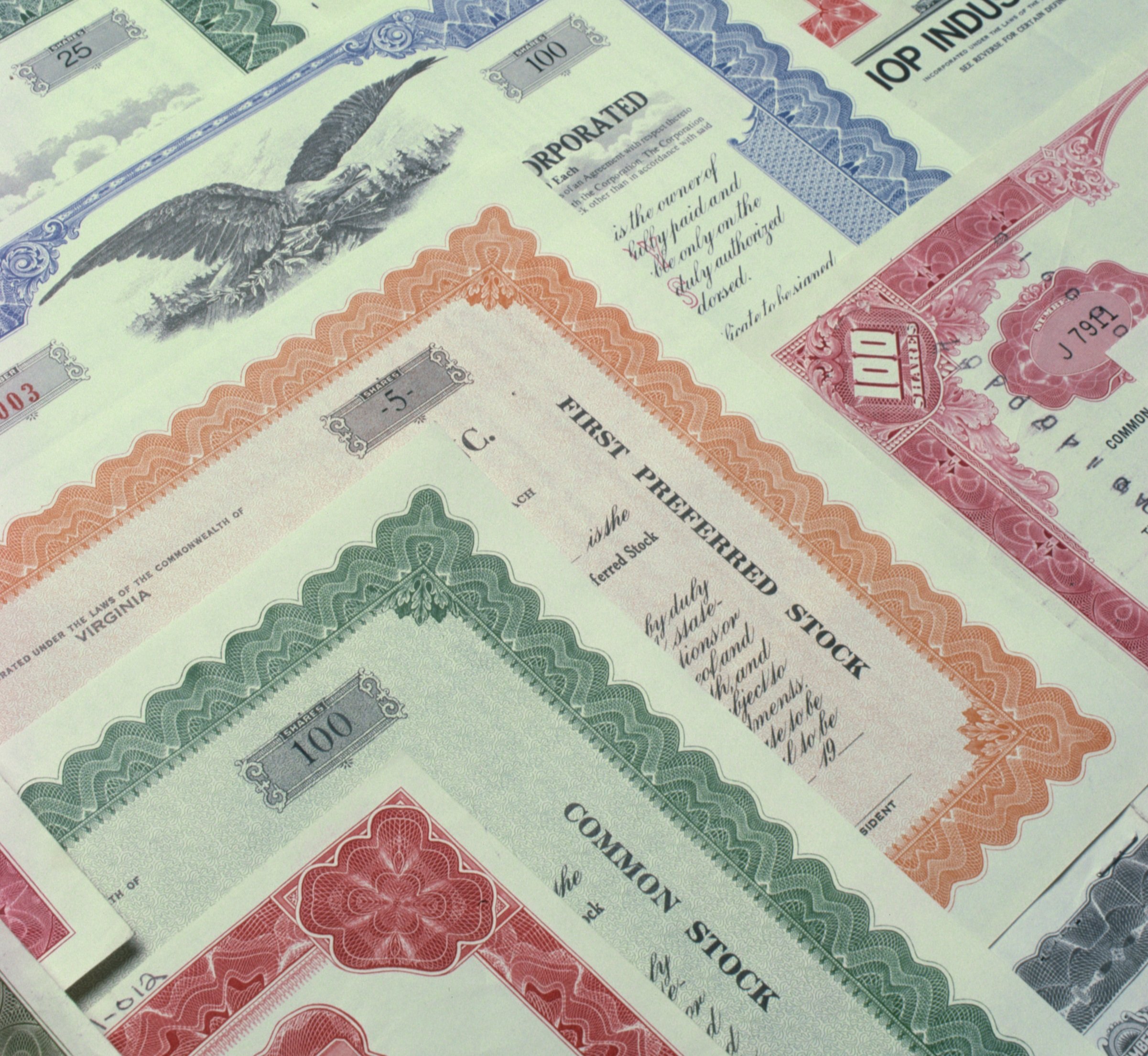 About a dozen stock certificates in different colors overlapping each other.