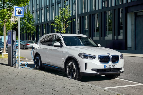 A white BMW iX3, a compact electric crossover SUV, at a roadside charging station 