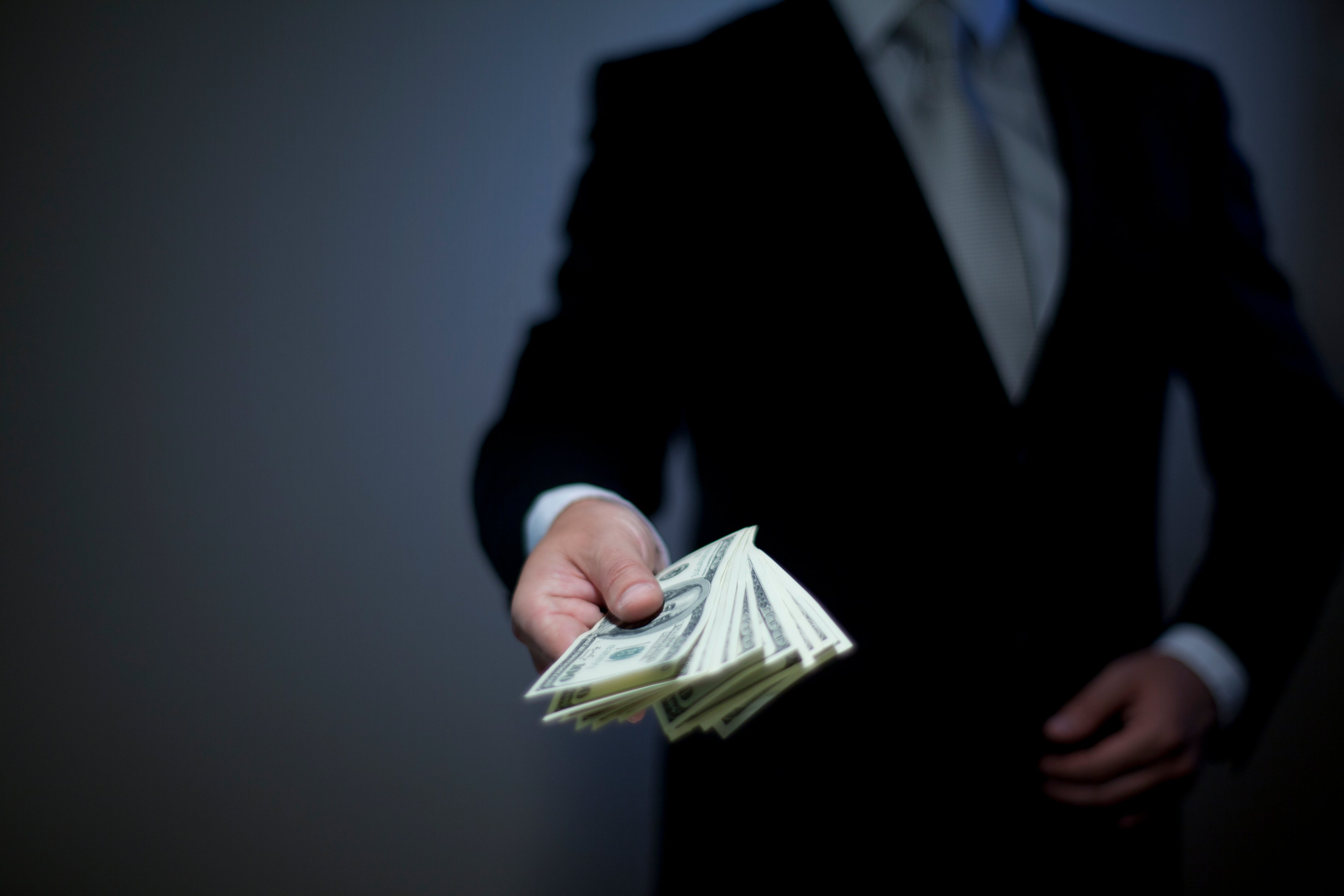 A person in a suit handing over a stack of cash.