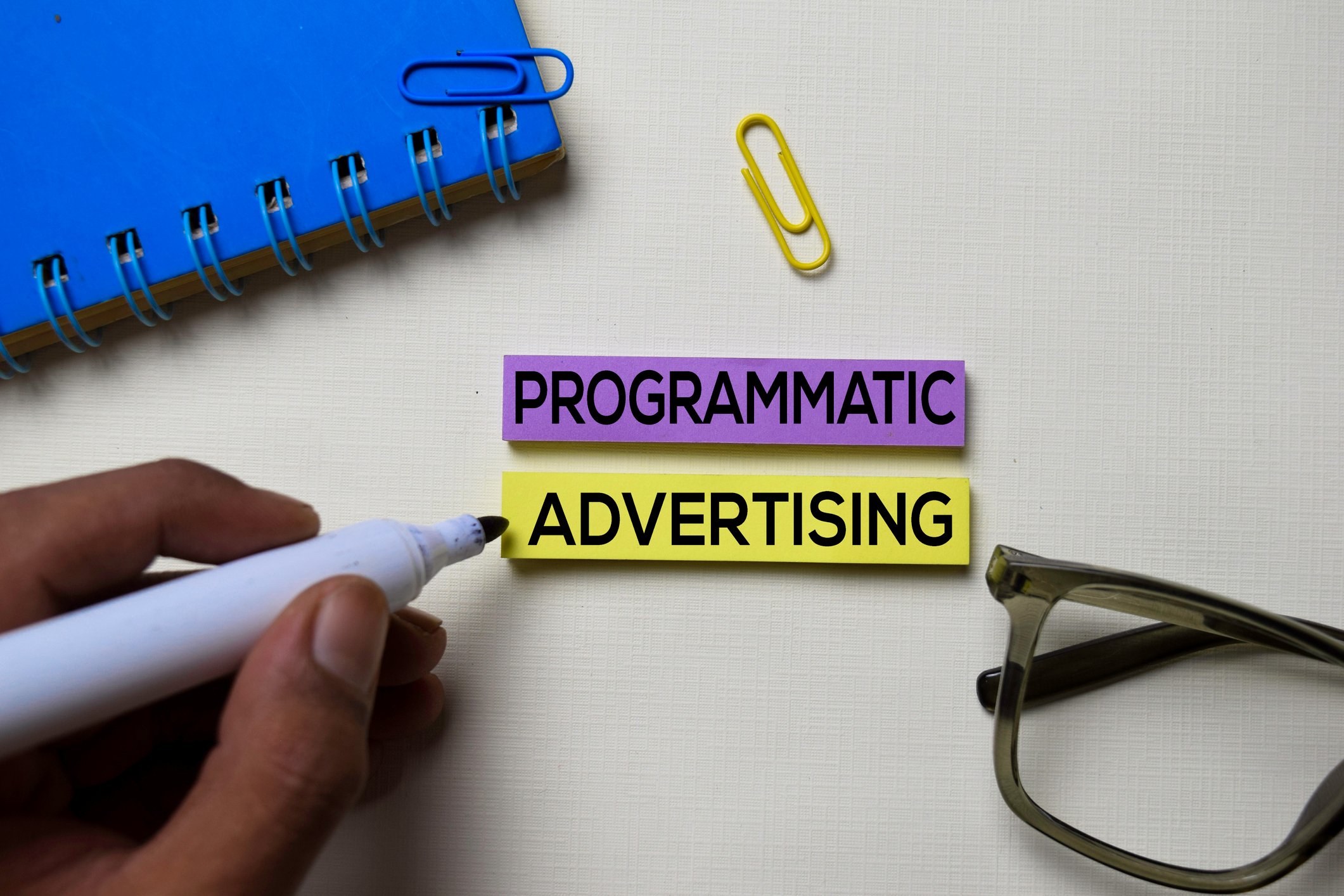 A magic marker writes on two strips of paper the words programmatic advertising. 