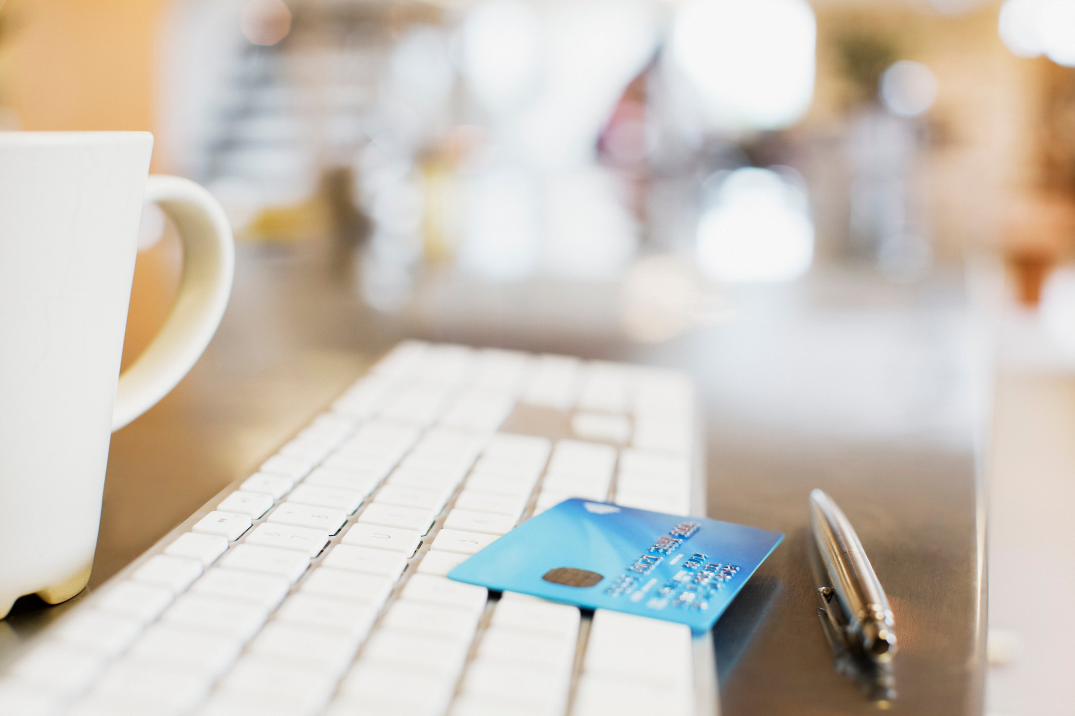 Keyboard with credit card and pen, with coffee cup nearby.
